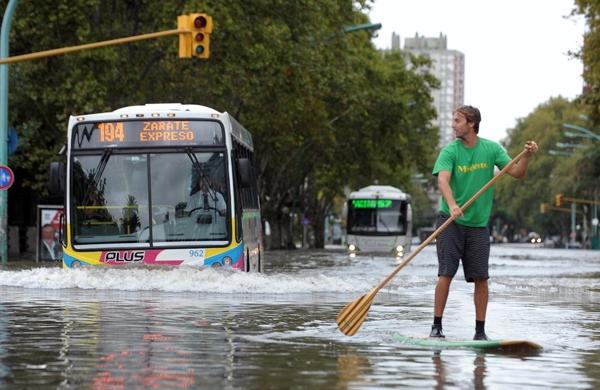 Argentino improvisa com prancha para se locomover em rua alagada, em Buenos Aires (France Press)