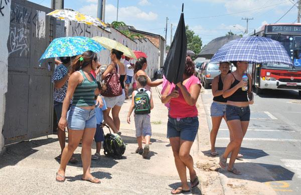 Mães na saída da escola com sombrinhas, muito calor. (Dominique Torquato/AAN)
