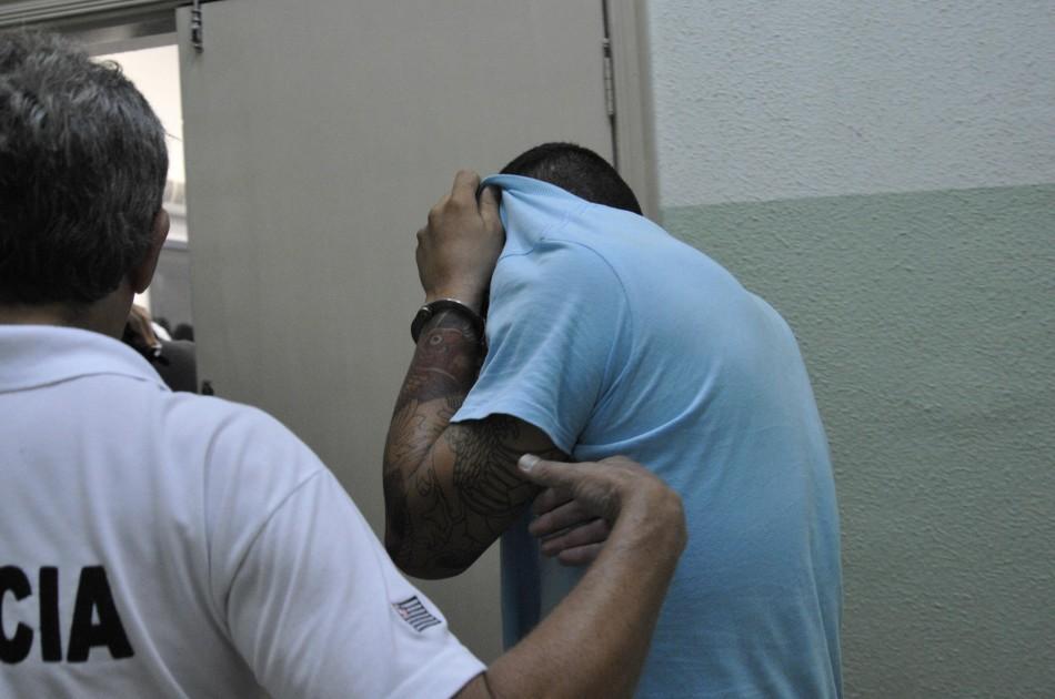 Um dos homens presos suspeitos pelos furtos esconde o rosto na delegacia (Sérgio Masson/AAN)