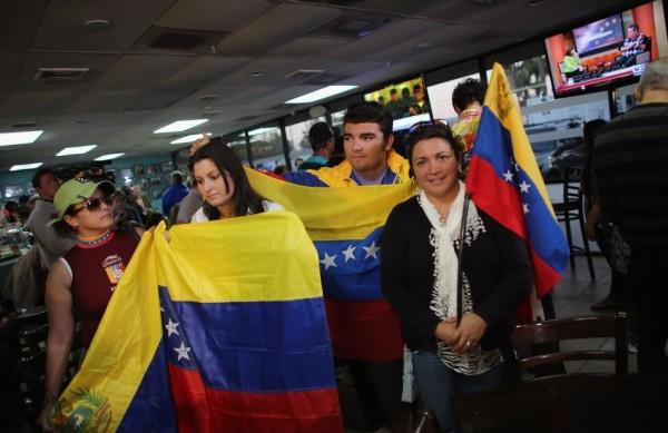 Viajantes seguram bandeira venezuelana enquanto escutam a notícia da morte de Chávez no aeroporto de Miami (EUA) (France Press)