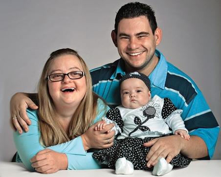 Descrição da imagem: foto de um jovem casal, ambos com síndrome de Down, e sua filhinha, ainda nenê, sem Síndrome de Down (Tô Dentro!)
