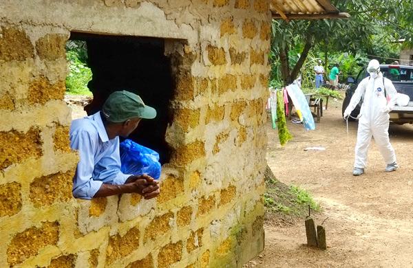 Homem olha para um m&eacute;dico da Cruz Vermelha da Lib&eacute;ria durante desinfec&ccedil;&atilde;o de uma &aacute;rea na pequena cidade de Banjol, onde tr&ecirc;s pessoas infectadas com o v&iacute;rus Ebola morreram nesta sexta (5) (DOMINIQUE FAGET/ AFP)