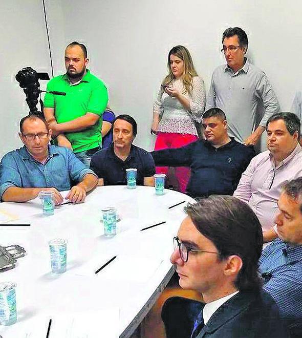 Eduardo e Renato, sentados ao fundo, de camisas azul-escuras, acompanham reunião para selar acordo (Divulgação)