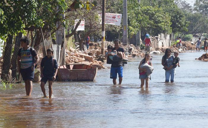 Adultos e crian&ccedil;as passam por rua inundada na cidade de Assun&ccedil;&atilde;o, no Paraguai (France Press)