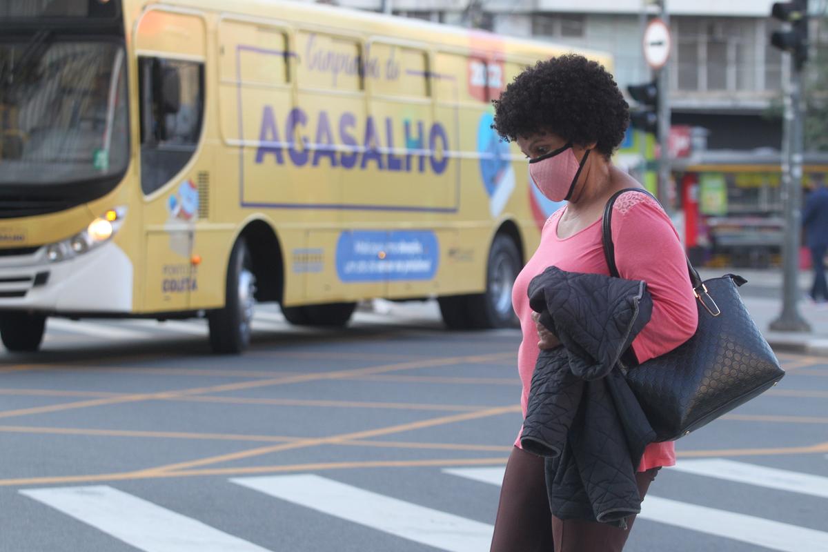 Mulher com o casaco nos braços, enquanto ônibus do transporte público, ao fundo, alerta para a Campanha do Agasalho deste ano, lançada pela Prefeitura na última sexta-feira (Ricardo Lima)