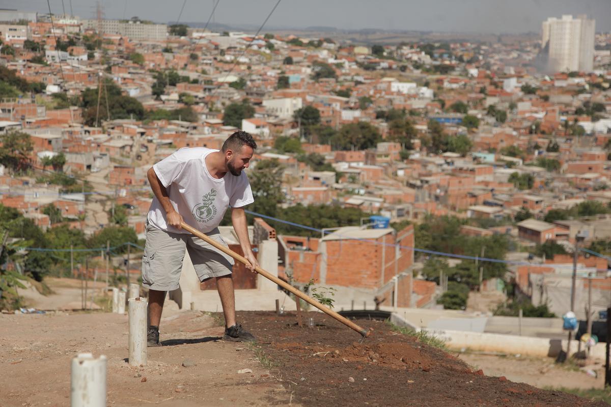 Luan José Tierri de Sousa prepara o solo para plantar árvores frutíferas, tendo ao fundo o Jd. Monte Cristo (Kamá Ribeiro)