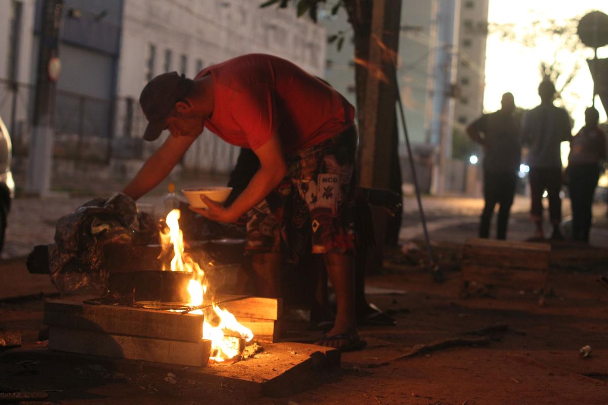 Morador de rua esquenta comida em ‘fogão’ improvisado montado em praça na Vila Industrial, onde grupos de pessoas em situação vulnerável se aglomeram (Ricardo Lima)