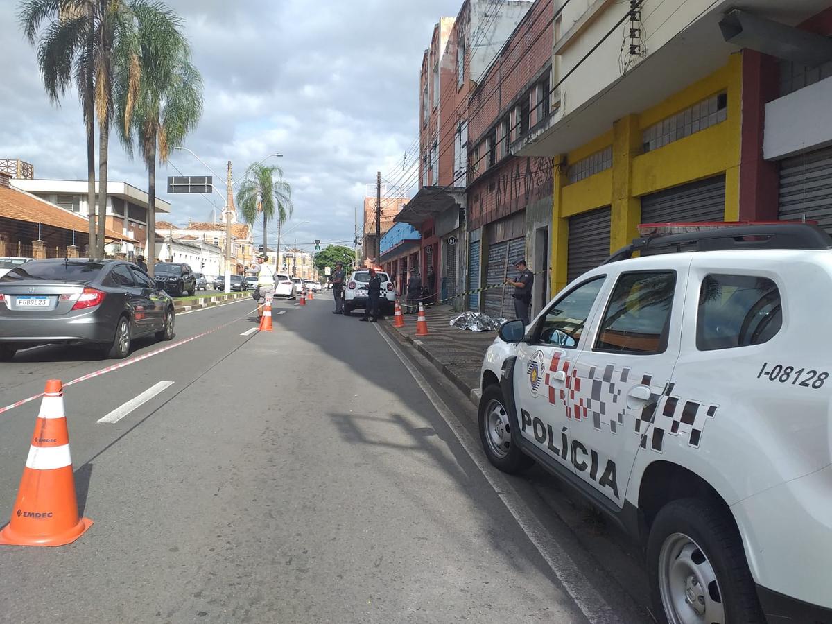 Corpo coberto da vítima na Avenida Andrade Neves aguarda, sob a vigilância de PM, transporte ao IML (Alenita Ramirez)