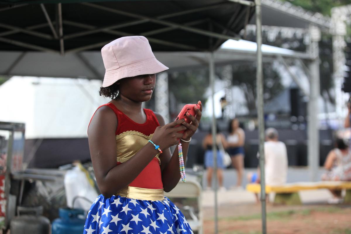Foliã consulta mensagens em seu celular enquanto aguarda o início do desfile de um bloco de carnaval (Kamá Ribeiro)