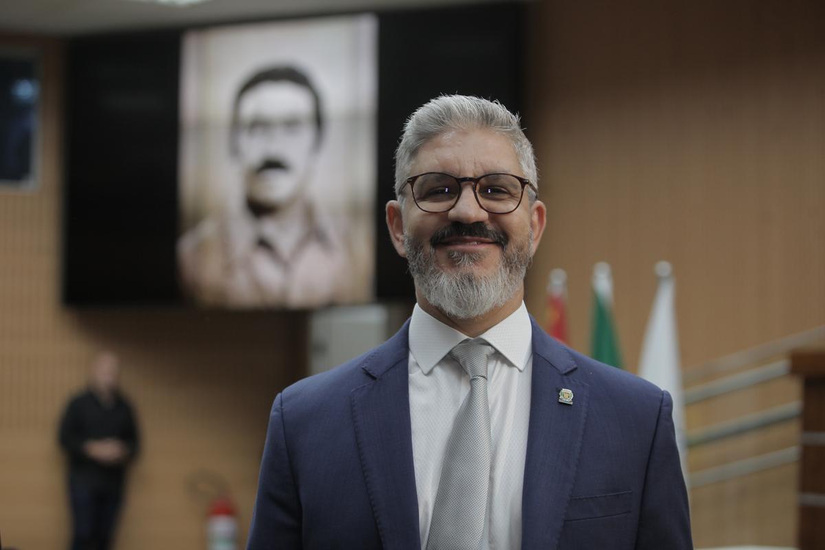 Peter Panutto, atual secretário municipal de Justiça, sorri em primeiro plano com a foto do pai ao fundo (Kamá Ribeiro)