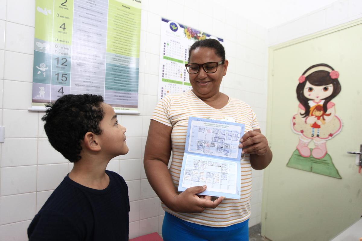 A mãe Patricia Martins mostra a caderneta de vacinação atualizada do filho João Pedro, logo após ele receber o imunizante contra a gripe; adultos também podem colocar a imunização em dia nos centros de saúde (Kamá Ribeiro)