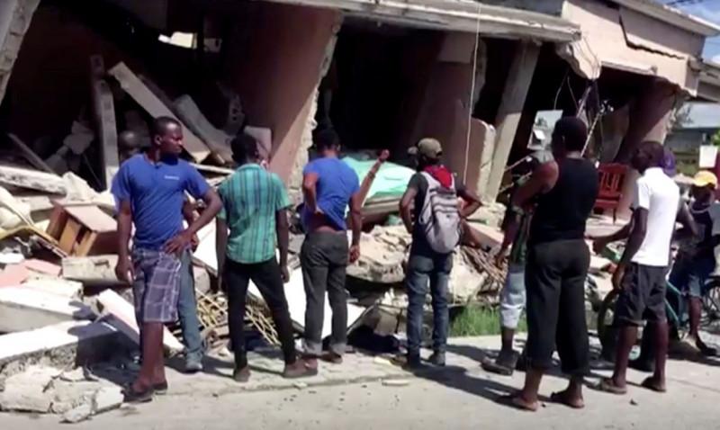 People stand in front of a collapsed building following an earthquake, in Les Cayes, Haiti, in this still image taken from a video obtained by Reuters on August 14, 2021.   REUTERS TV via REUTERS THIS IMAGE HAS BEEN SUPPLIED BY A THIRD PARTY. MANDATORY CREDIT. (REUTERS TV)