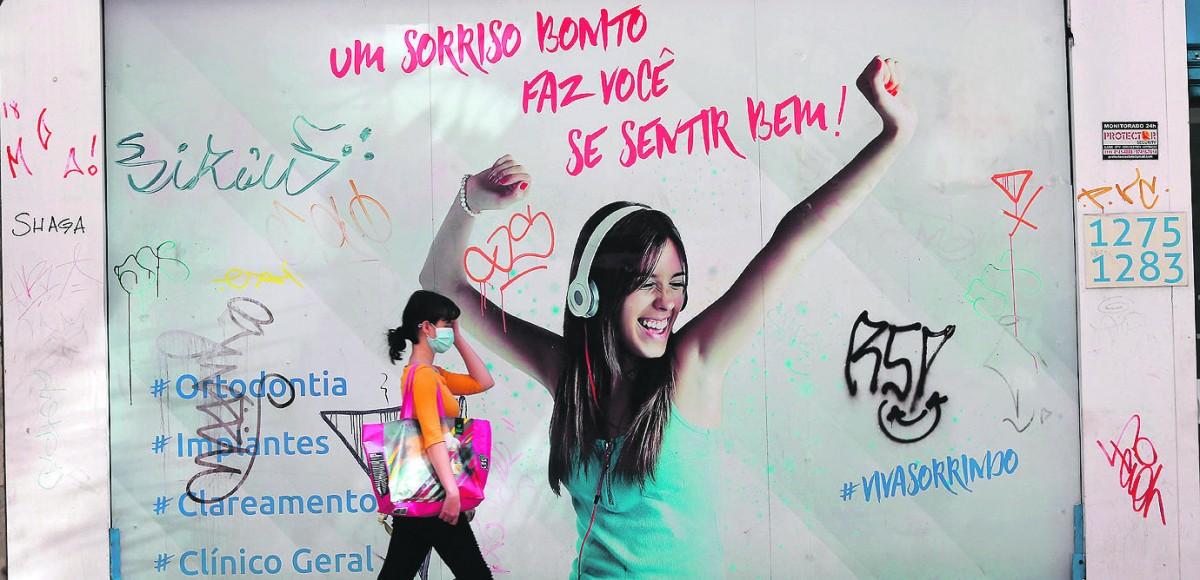 Entre a placa publicitária e os garranchos da pichação, no Centro, jovem segue o seu caminho devidamente protegida (LEANDRO FERREIRA/AAN)