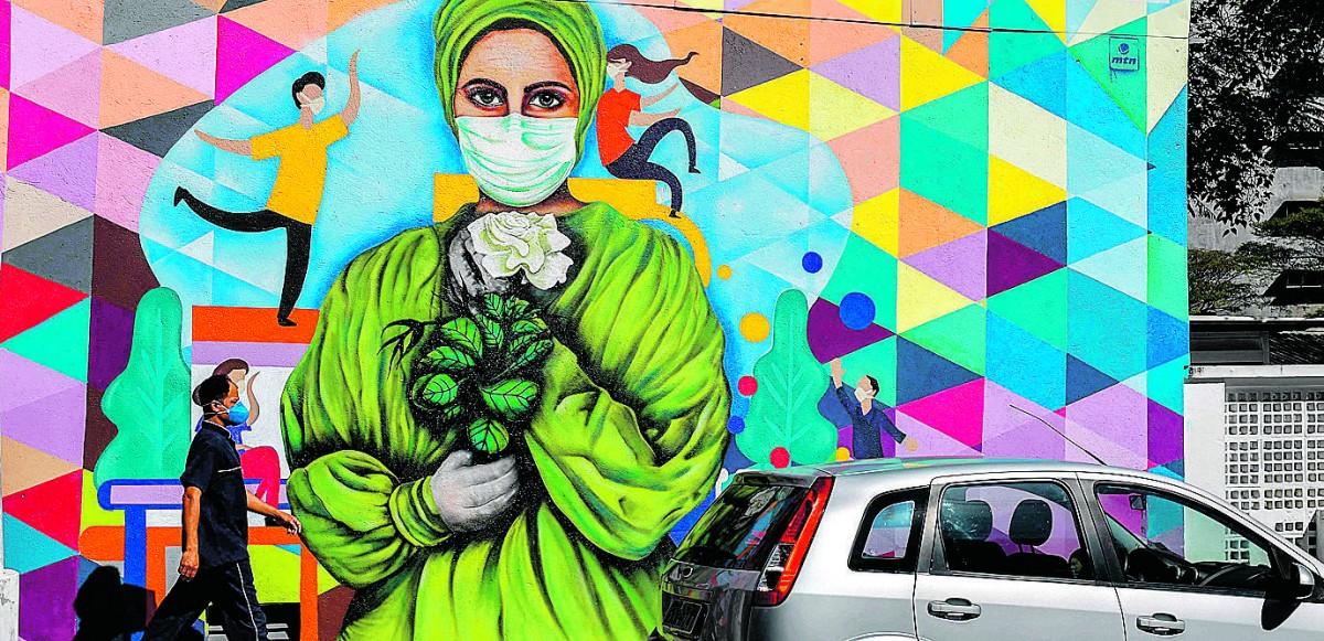 Funcionário protegido passa por painel em rua paulistana que acolhe a pandemia com um simbólico buquê (Nelson Almeida/France Press)