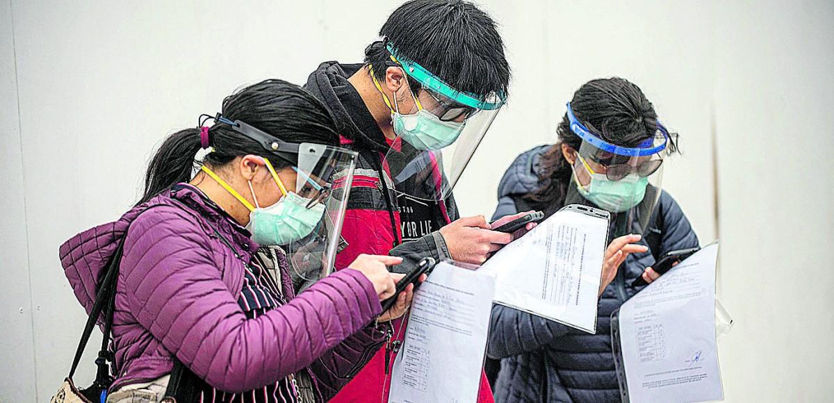 Com máscaras e frontal de acrílico, passageiros conferem informações de embarque no aeroporto de Lima (ERNESTO BENAVIDES/FRANCE PRESS)
