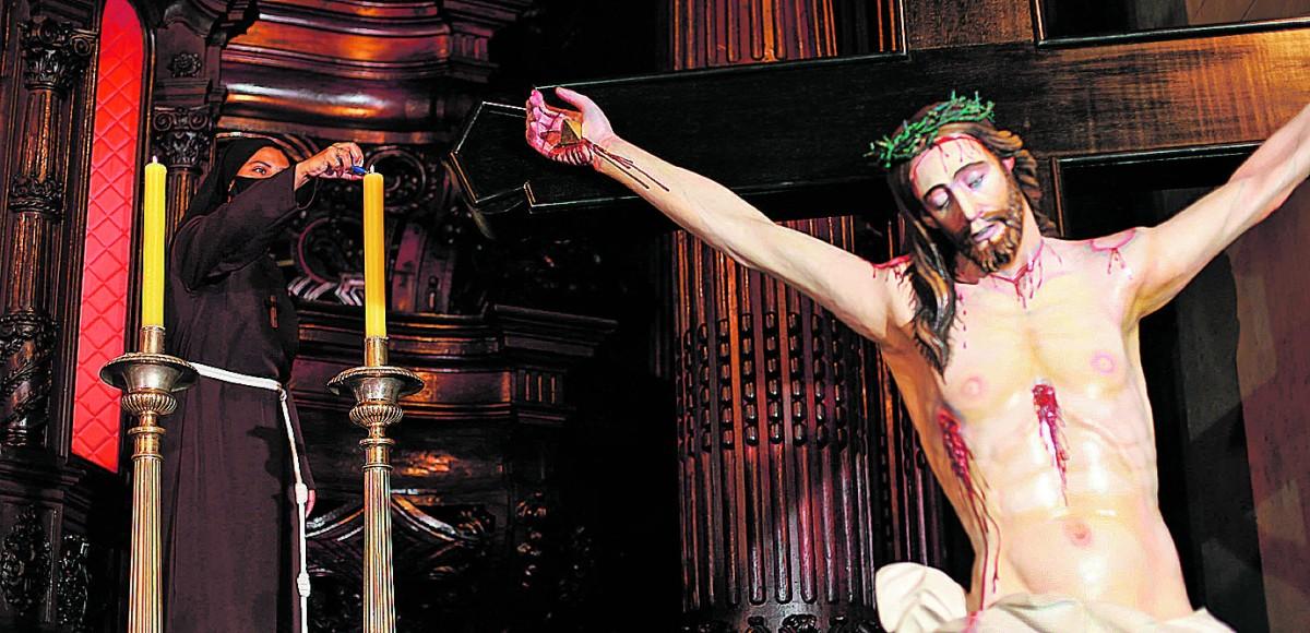 Auxiliar de uma ordem religiosa acende vela próximo ao altar da Catedral Metropolitana, ao lado de Jesus crucificado (Leandro Ferreira/AAN)