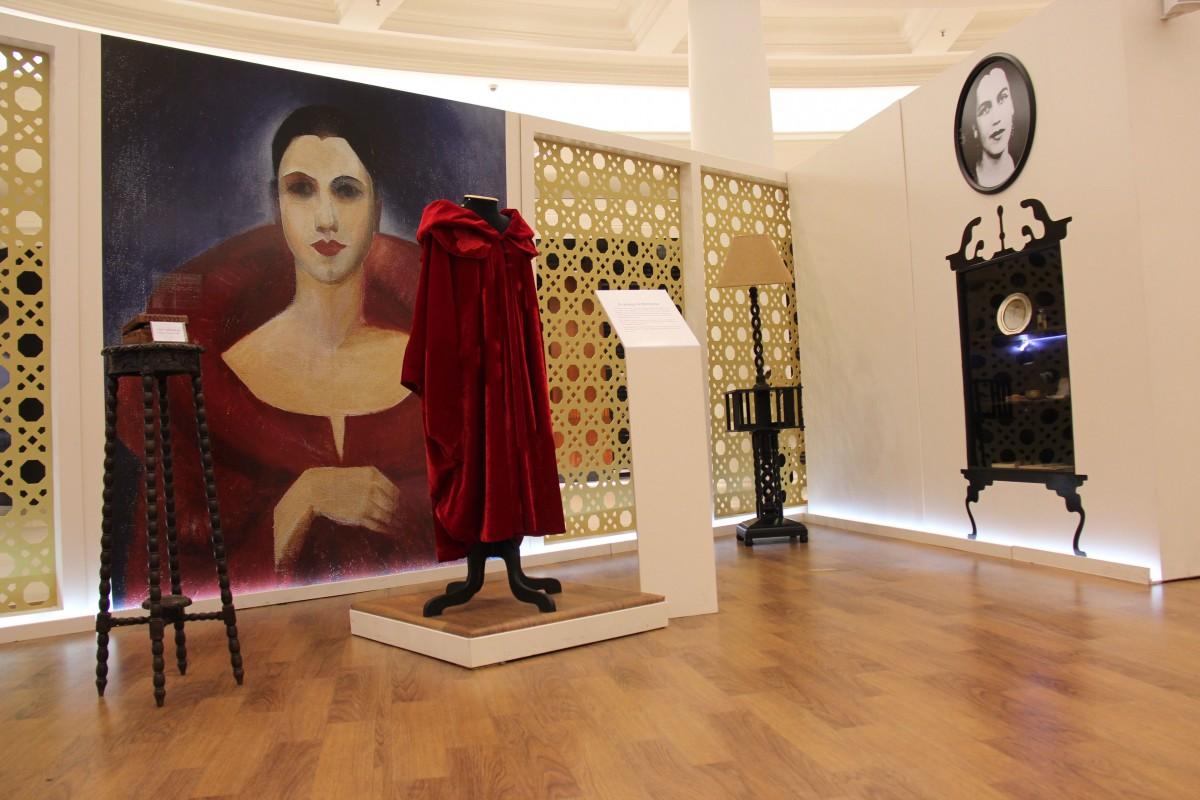 Ambiente da exposição 'Universo de Tarsila' que mostra vestido usado pela artista, representada em autorretrato ao fundo, e outros objetosr
 (DIVULGAÇÃO)