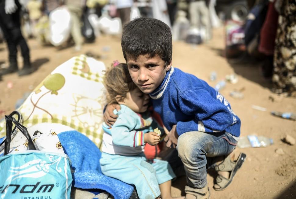 Menino segura beb&ecirc; como os curdos s&iacute;rios, fugindo de ataque pelo Estado Isl&acirc;mico jihadista (EI) do grupo, antes de tentar atravessar a fronteira entre a S&iacute;ria e Turquia  (BULENT KILIC/ AFP)